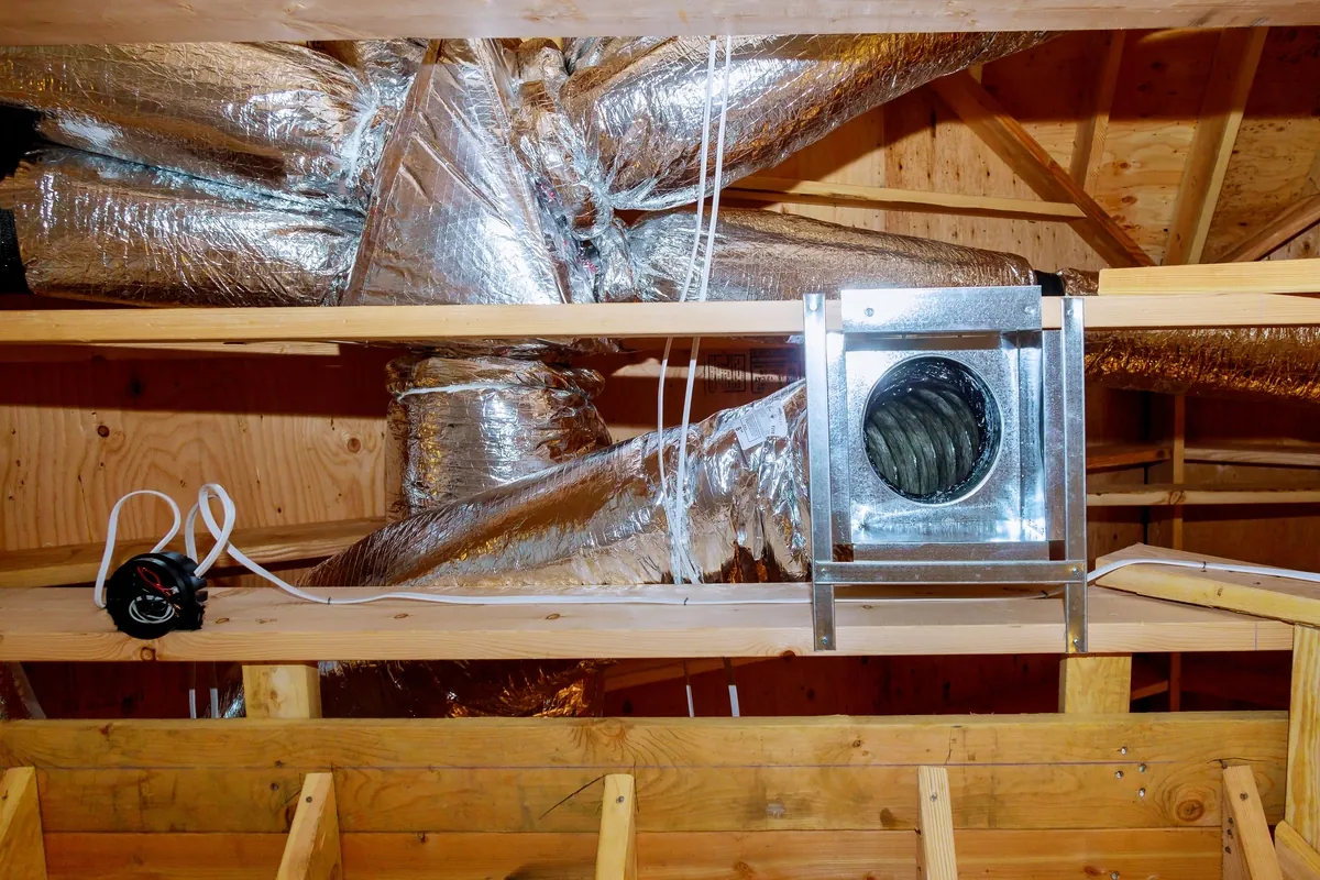 A professionally installed attic ventilation system in a Los Angeles home, featuring foil-insulated ductwork and precision metal fittings secured between wooden beams.