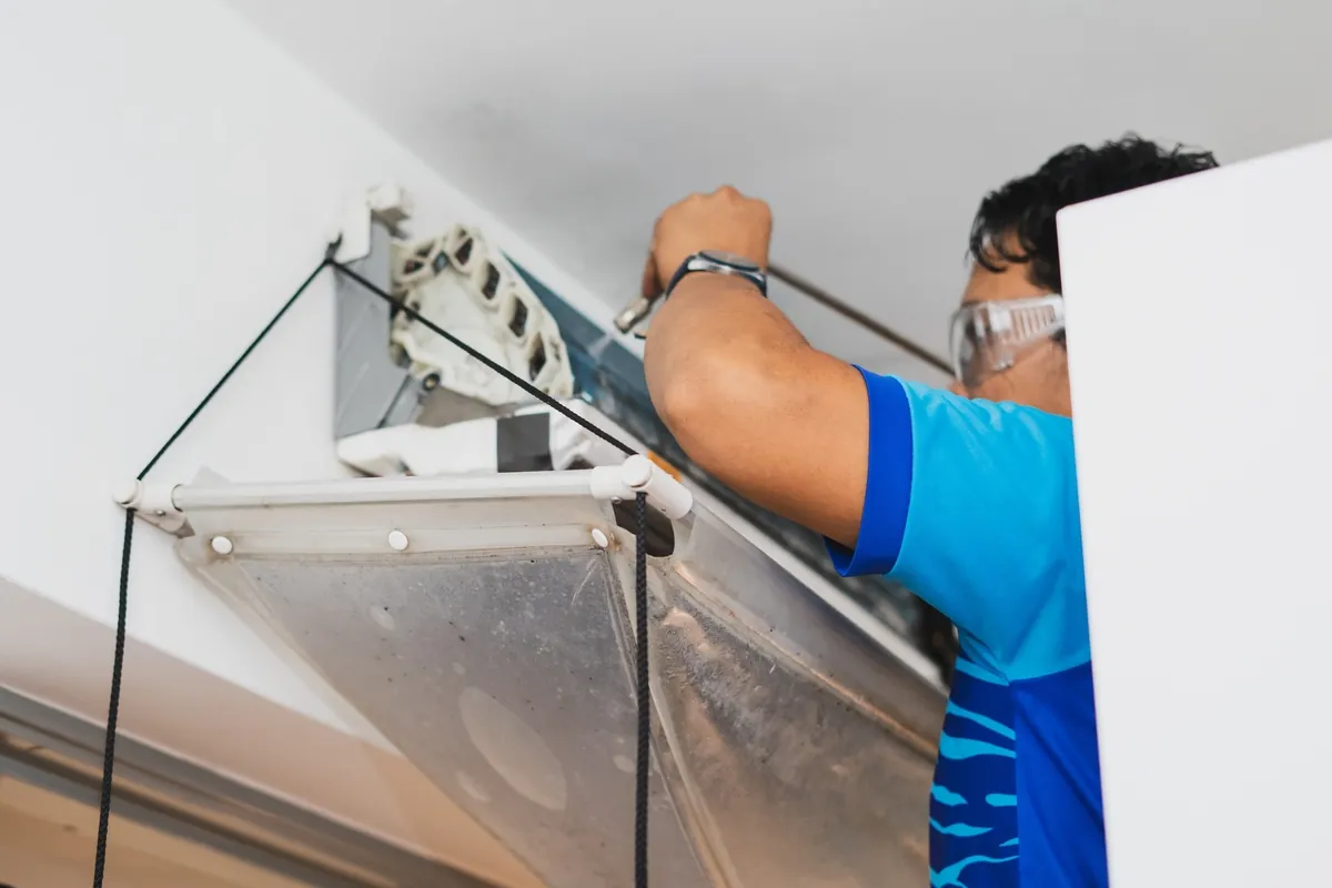Professional HVAC technician in a blue shirt performing an air conditioner safety inspection and maintenance check in a Los Angeles home to ensure energy efficiency.