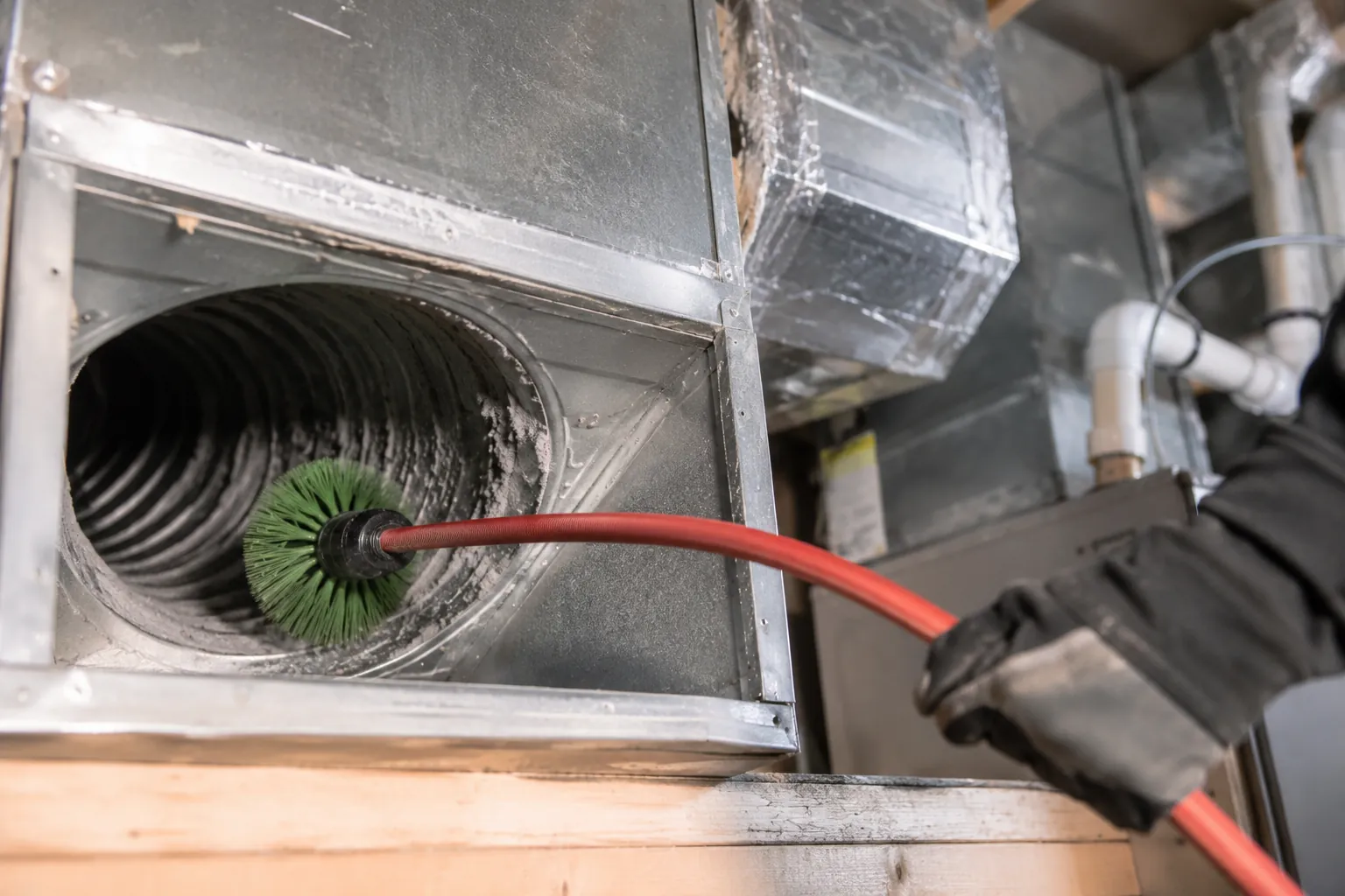 A professional technician using a high-reach rotary brush to remove mold and contaminants from the main HVAC trunk line in a Los Angeles home.
