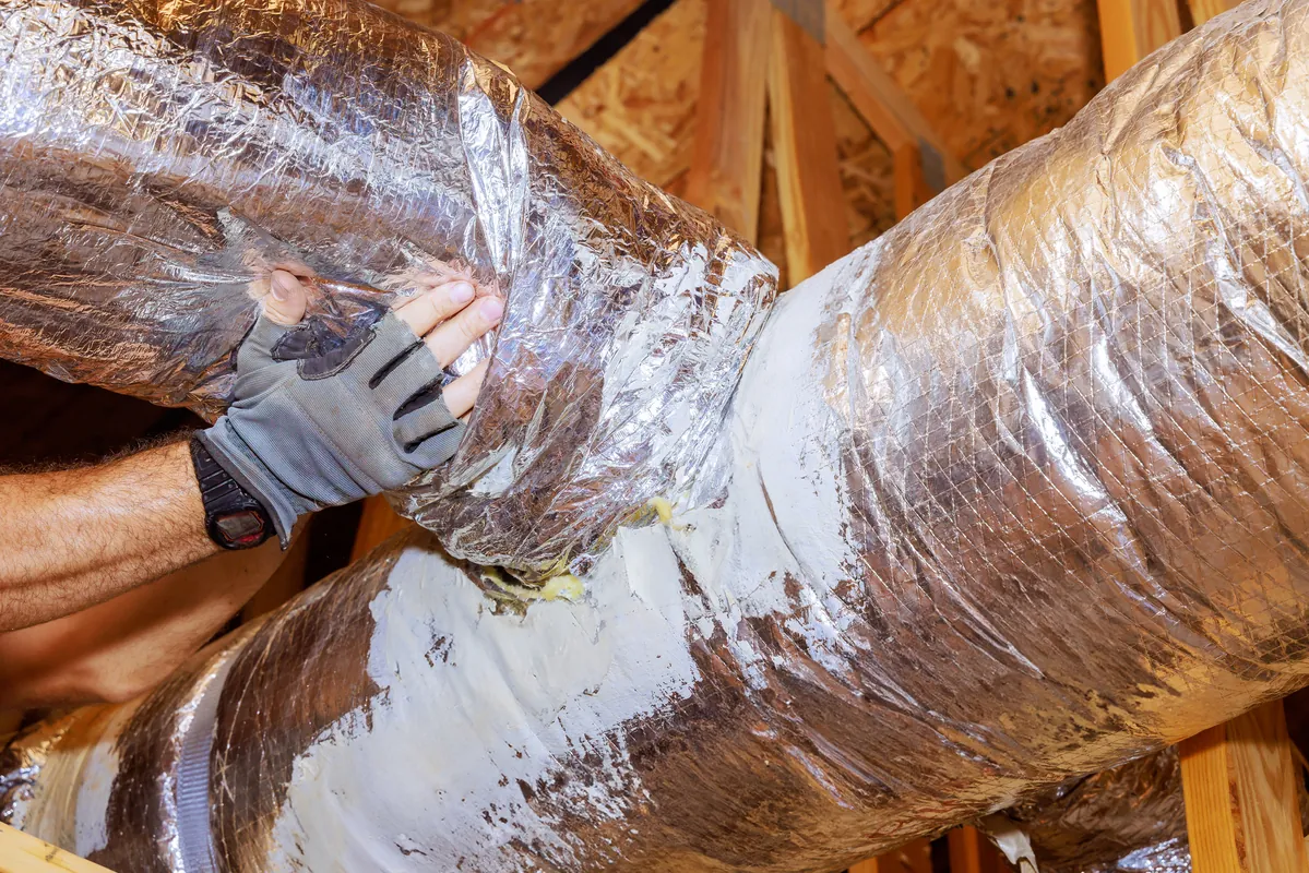 A professional technician sealing insulated flexible ductwork with specialized mastic paste to prevent air leaks in a Los Angeles attic.