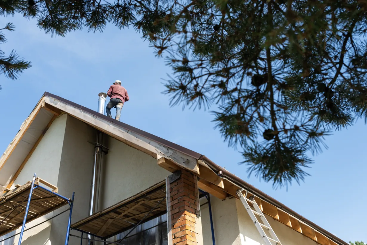 Professional chimney technician performing an annual maintenance inspection on a residential metal flue in Southern California, utilizing safety scaffolding and ladders for a thorough rooftop service.