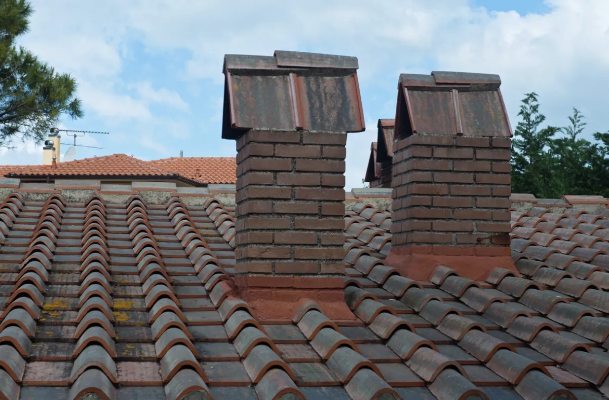 Group of brick chimneys on a Mediterranean-style tile roof in the San Fernando Valley, highlighting the need for specialized creosote removal and multi-flue cleaning services.