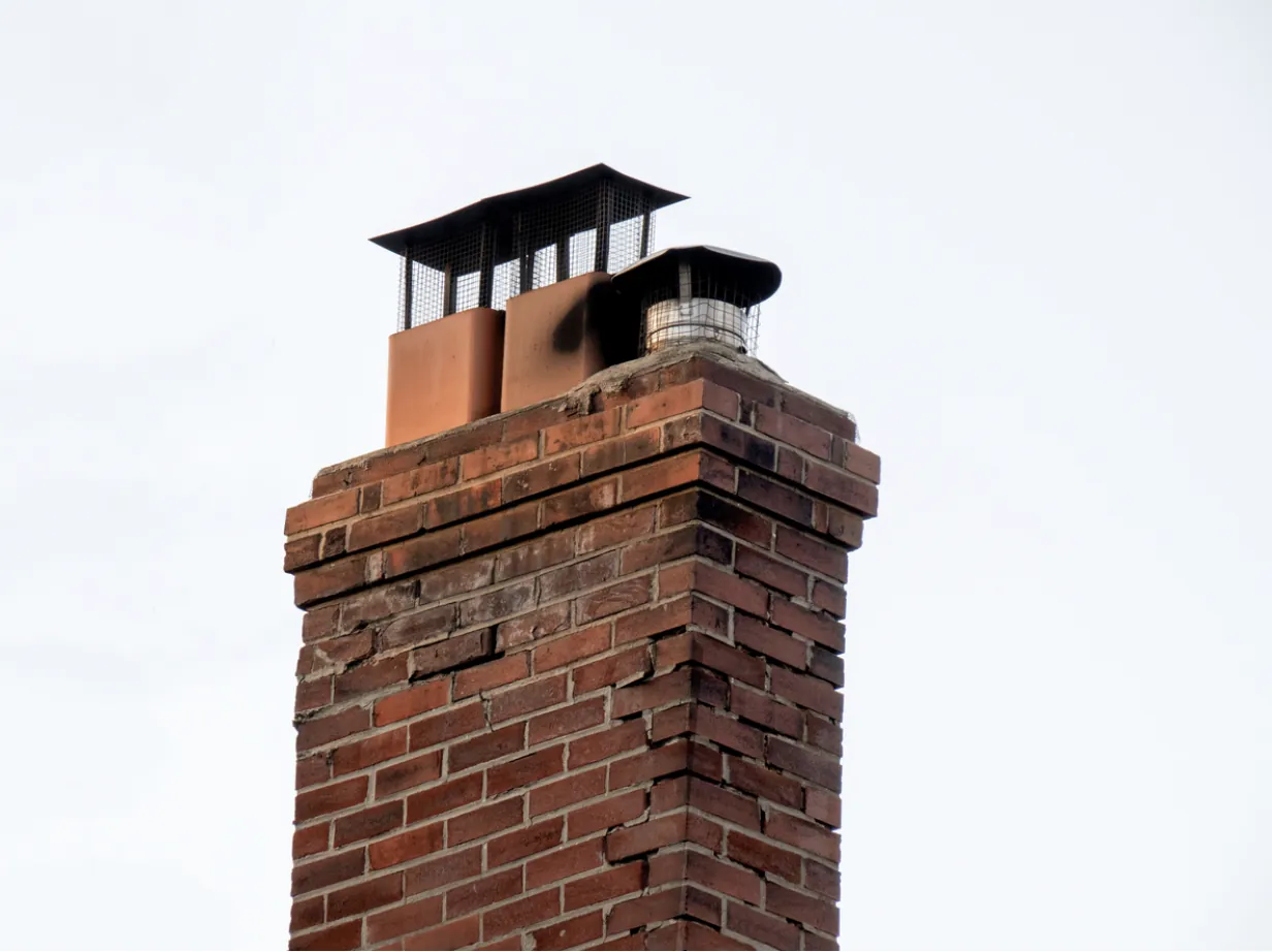 Inspection of an old brick chimney with three flues and custom fireplace spark arrestors in Los Angeles, focusing on creosote removal and wildfire prevention.
