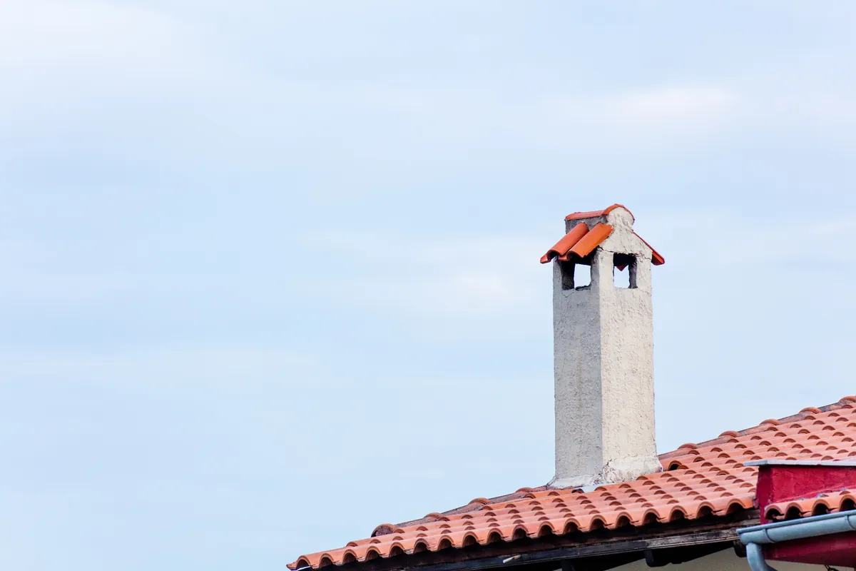 A gray stucco chimney rising above a terracotta tiled roof in Los Angeles, showing a chimney crown in need of professional sealing and repair.