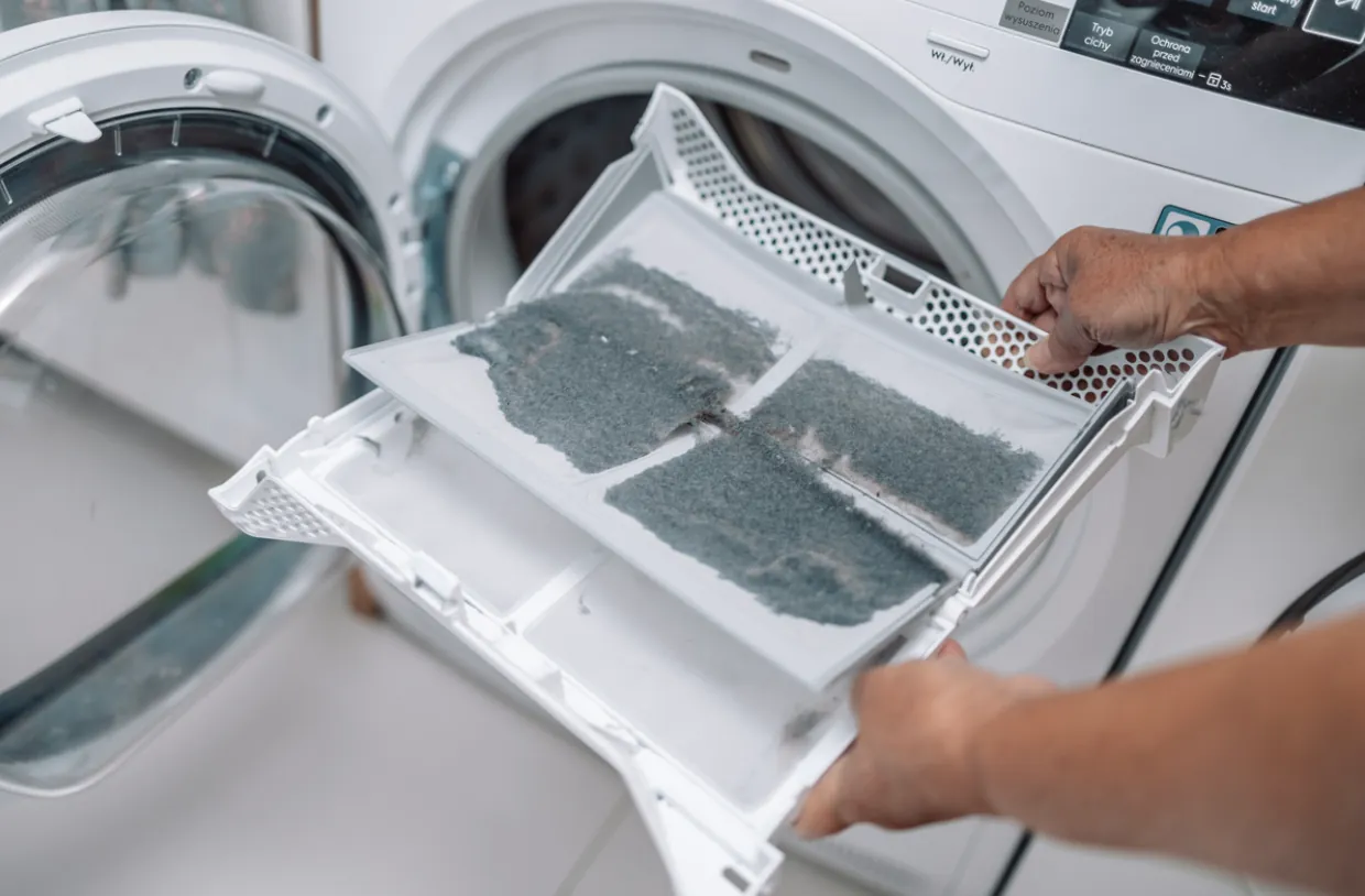 A person cleaning a dust-filled lint filter from a white clothes dryer to improve appliance efficiency in a Los Angeles home.