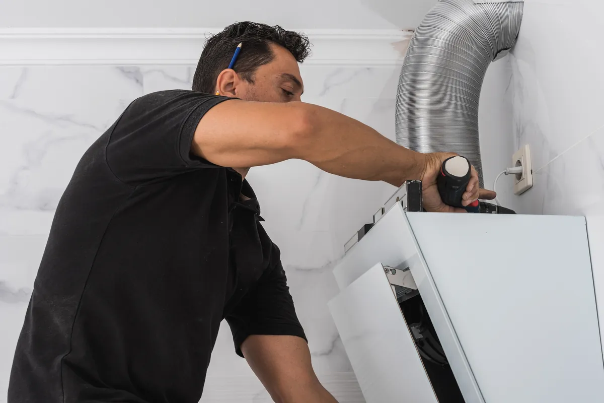 A professional technician installing a new white exterior vent hood and metal ducting for a residential dryer system in Los Angeles.