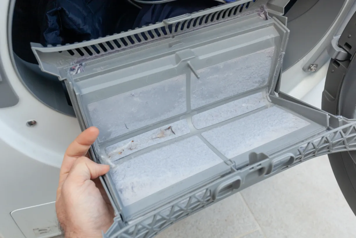 A close-up of a dirty lint filter being removed from a dryer to prevent airflow blockages and maintain home safety in Los Angeles.