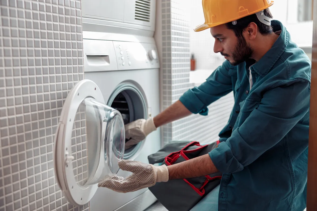 A professional repairman inspecting a stacked dryer unit for vent repair and maintenance services in Los Angeles.