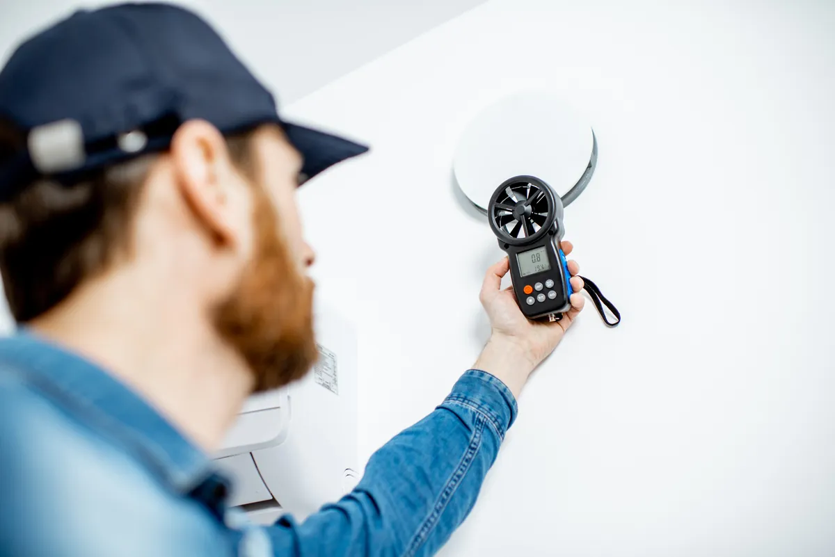 Professional technician in uniform performing maintenance on a workplace ceiling air conditioning unit in Los Angeles to ensure energy efficiency and optimal ventilation.
