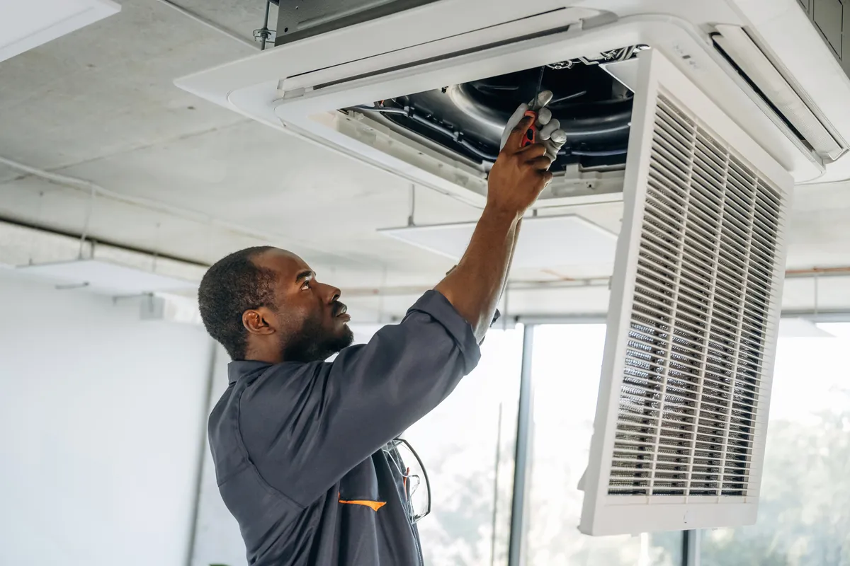 Professional technician in uniform performing maintenance on a workplace ceiling air conditioning unit in Los Angeles to ensure energy efficiency and optimal ventilation.