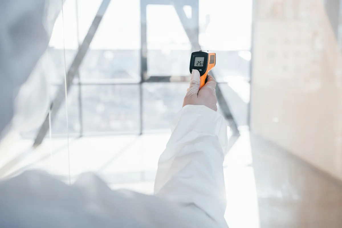 A technician in a protective suit using a digital monitoring device to perform indoor air quality testing and health protocol checks in a Los Angeles building.