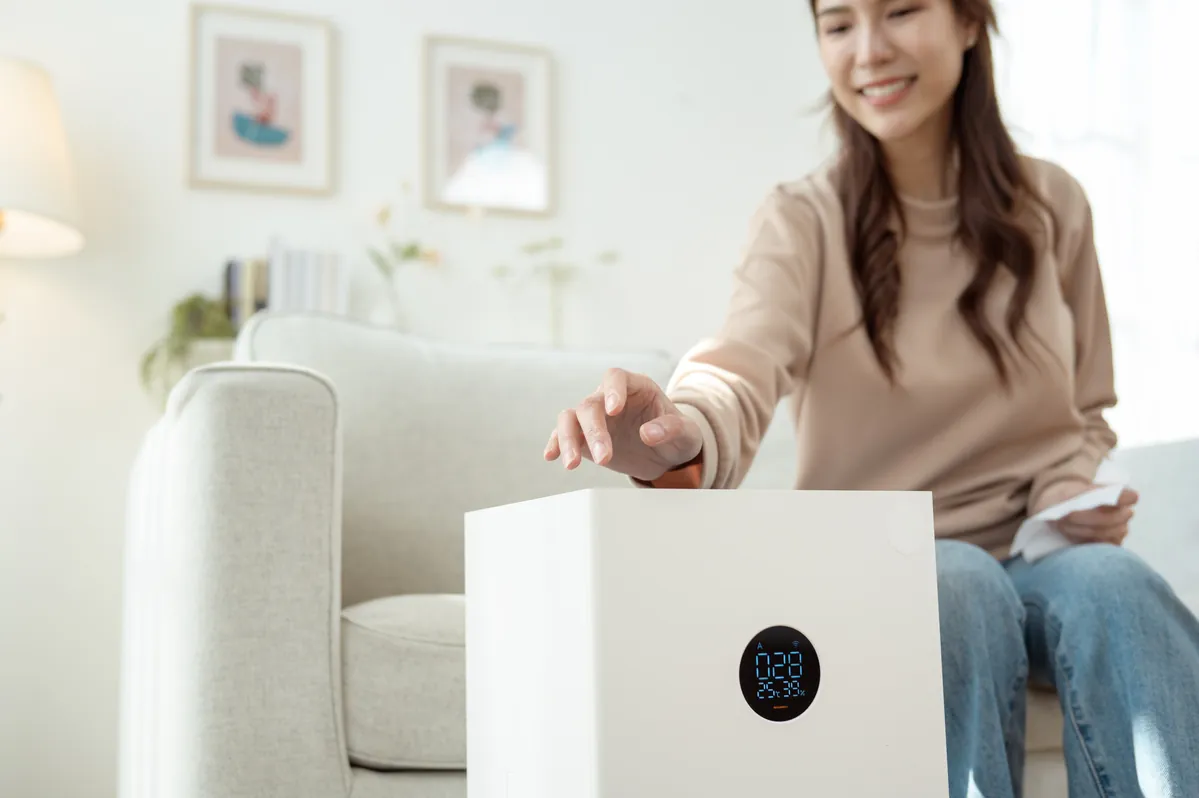 A woman in a Los Angeles home experiencing allergy relief and comfort next to a whole-home air purification system installed by SoCal Green Air and Chimney.